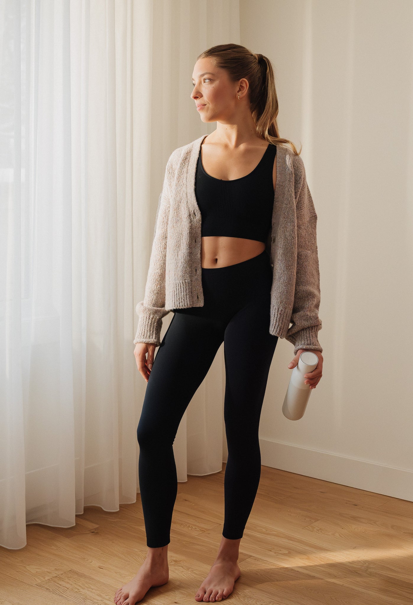 Femme debout de profil avec cardigan portant le legging long Sculpt Flow noir – Look lifestyle – Gamme SkinBloom – Soje Lingerie